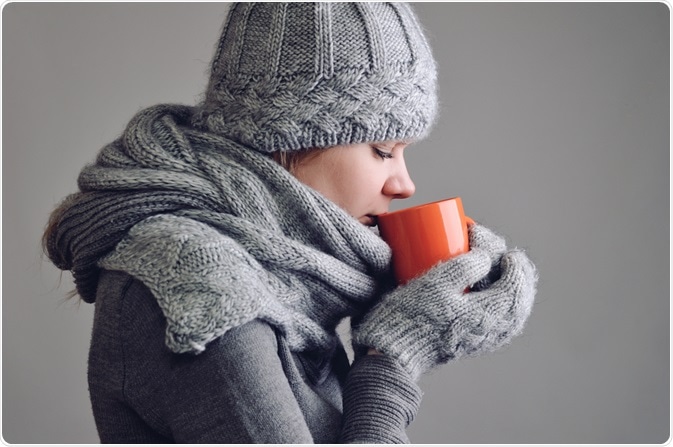 Woman drinking hot drink to prevent hypothermia/keep her core body temperature high - By morozv