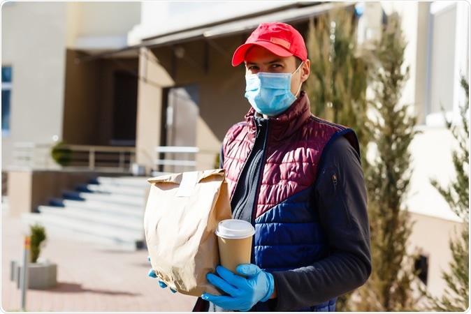 Courier in protective mask and gloves delivers takeaway food during covid-19 pandemic lockdown. Image Credit: Andrew Angelov / Shutterstock