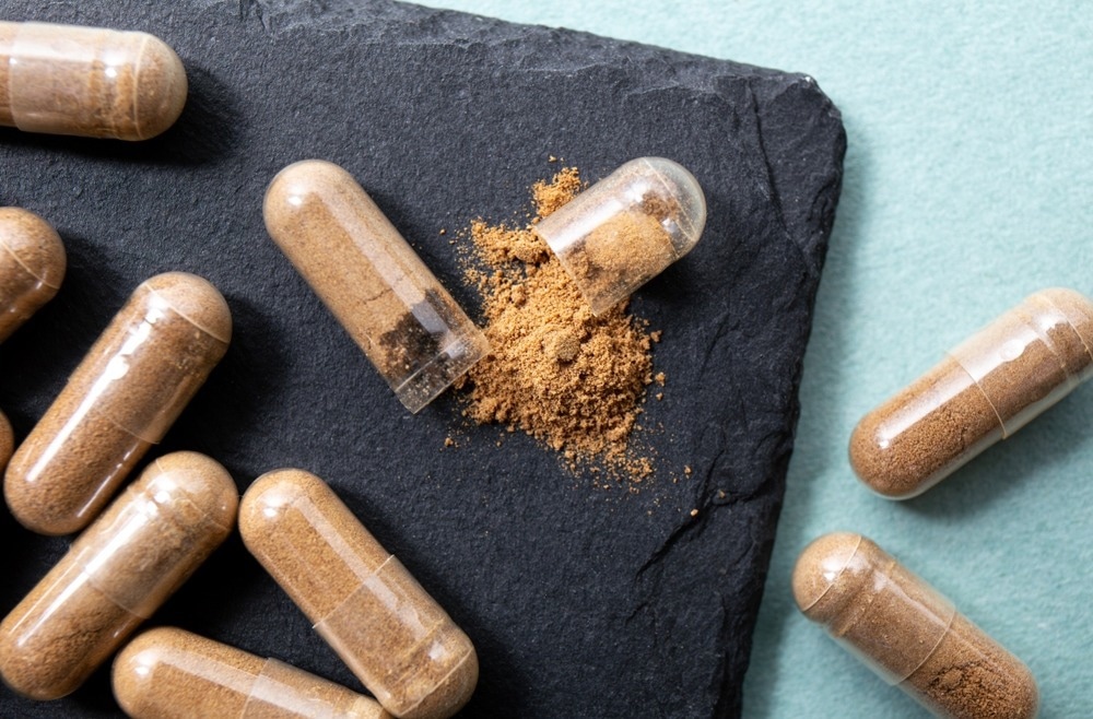 Ashwagandha root powder supplement capsules on black background.