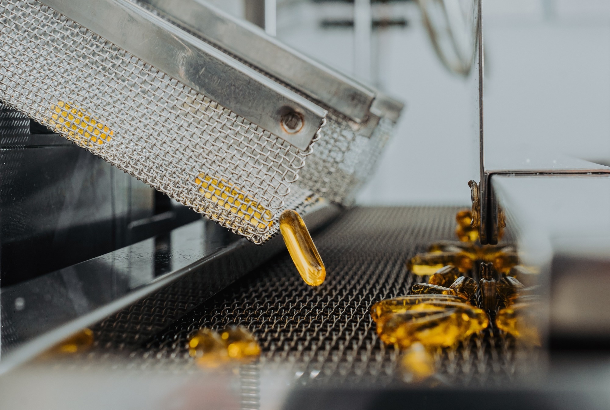 Yellow transparent capsules with oil moving down a conveyor belt.