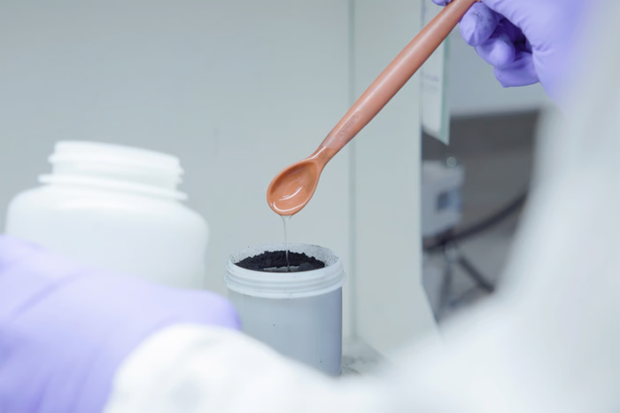 Gloved human hand holding scientific equipment, mixing materials to create a slurry.
