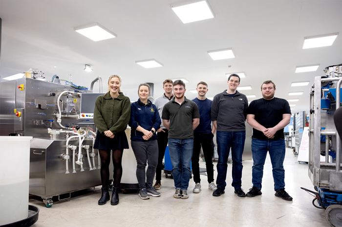 The Labman team stands in the centre of a lab, smiling at the camera.