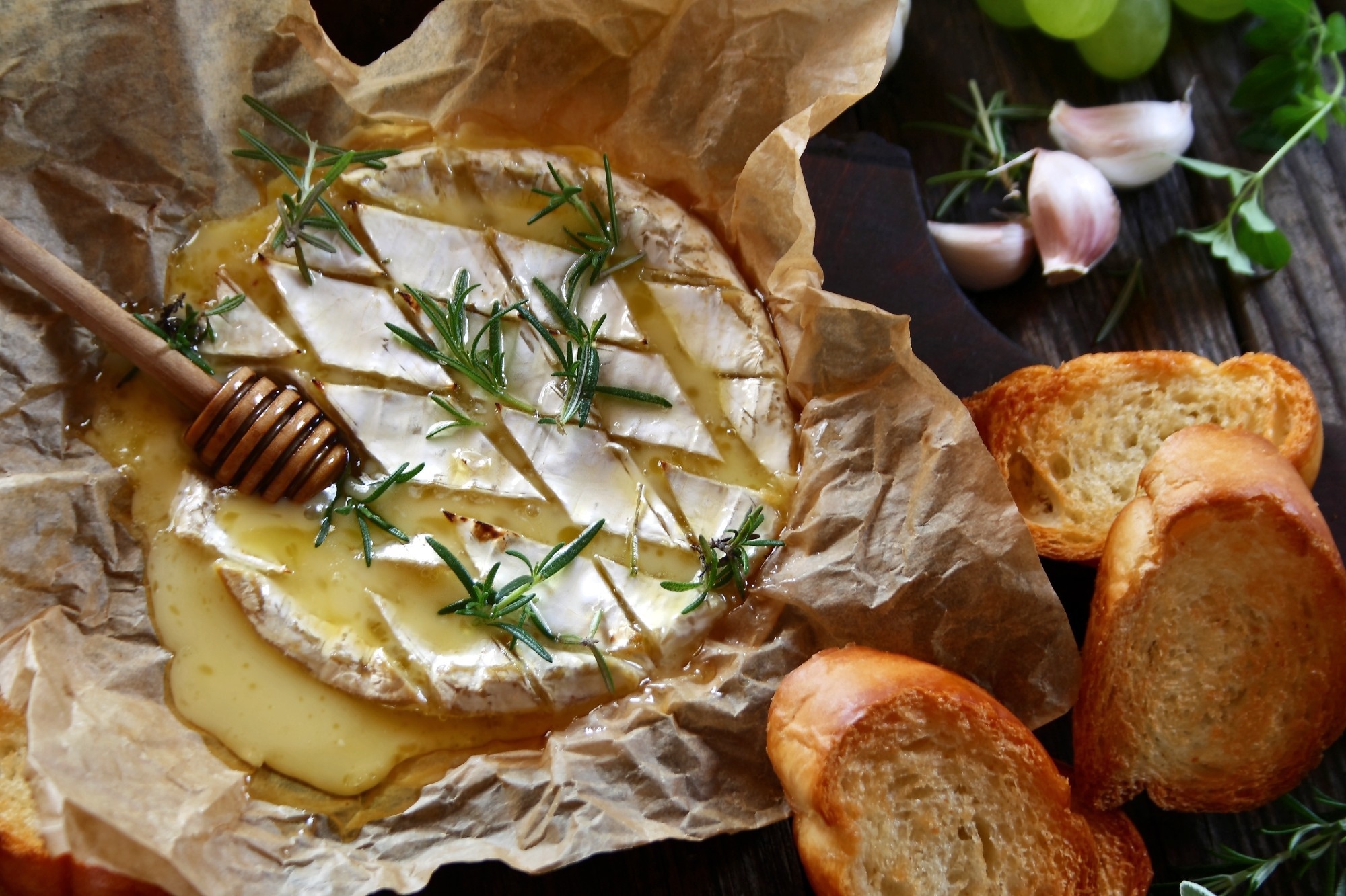 Baked camembert cheese with rosemary, garlic and honey on baking paper.