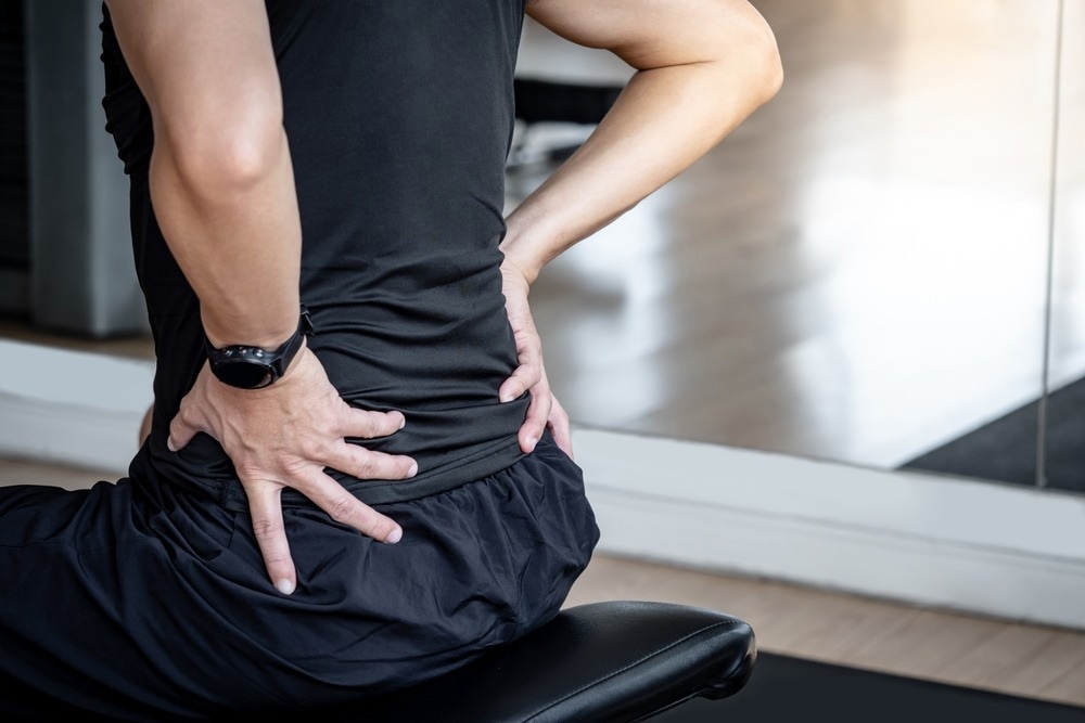 Sport man feeling lower back pain or spine pain while sitting on workout bench in fitness gym.