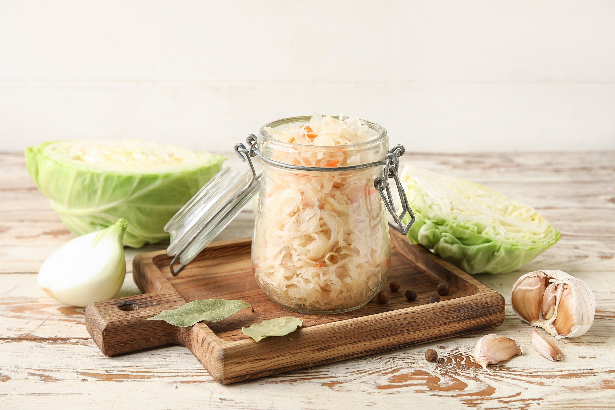 Jar with homemade sauerkraut on wooden tray and ingredients on wooden table.