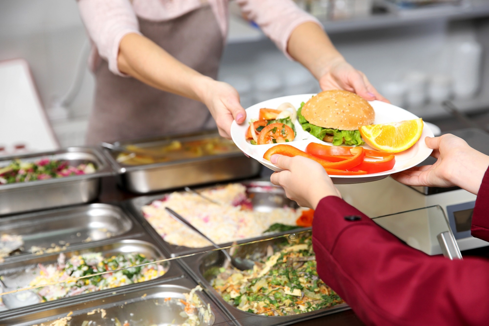 Pleasant woman giving lunch to school girl in cafeteria