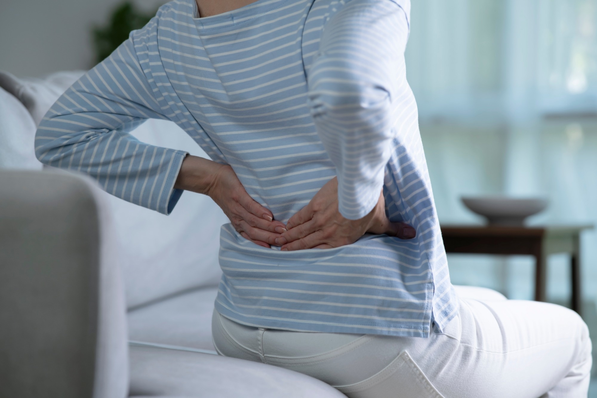 senior woman on sofa feeling and suffering from back pain and lower lumbar discomfort