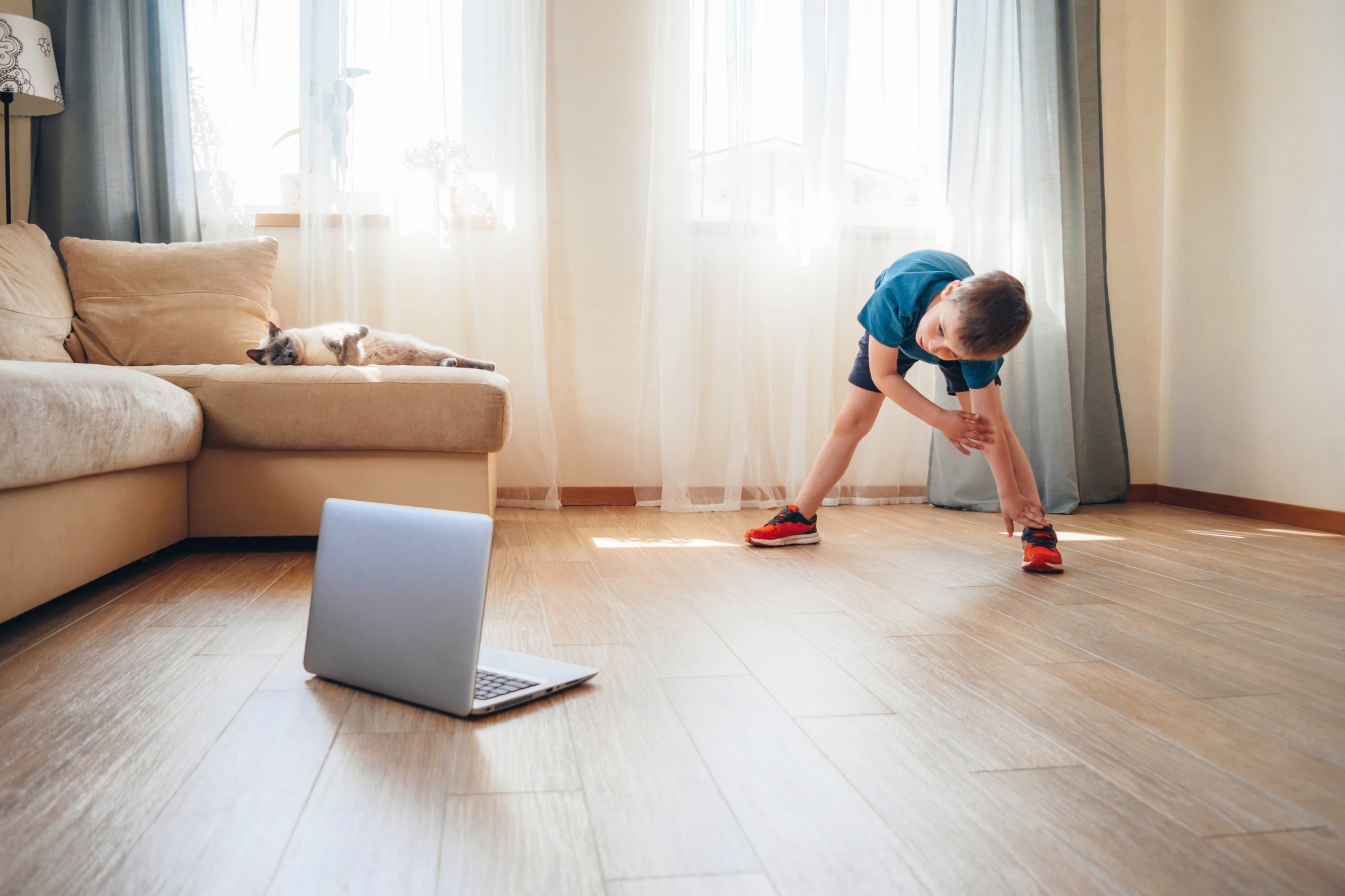 The boy doing physical exercises, watching video lesson online in front of open laptop computer