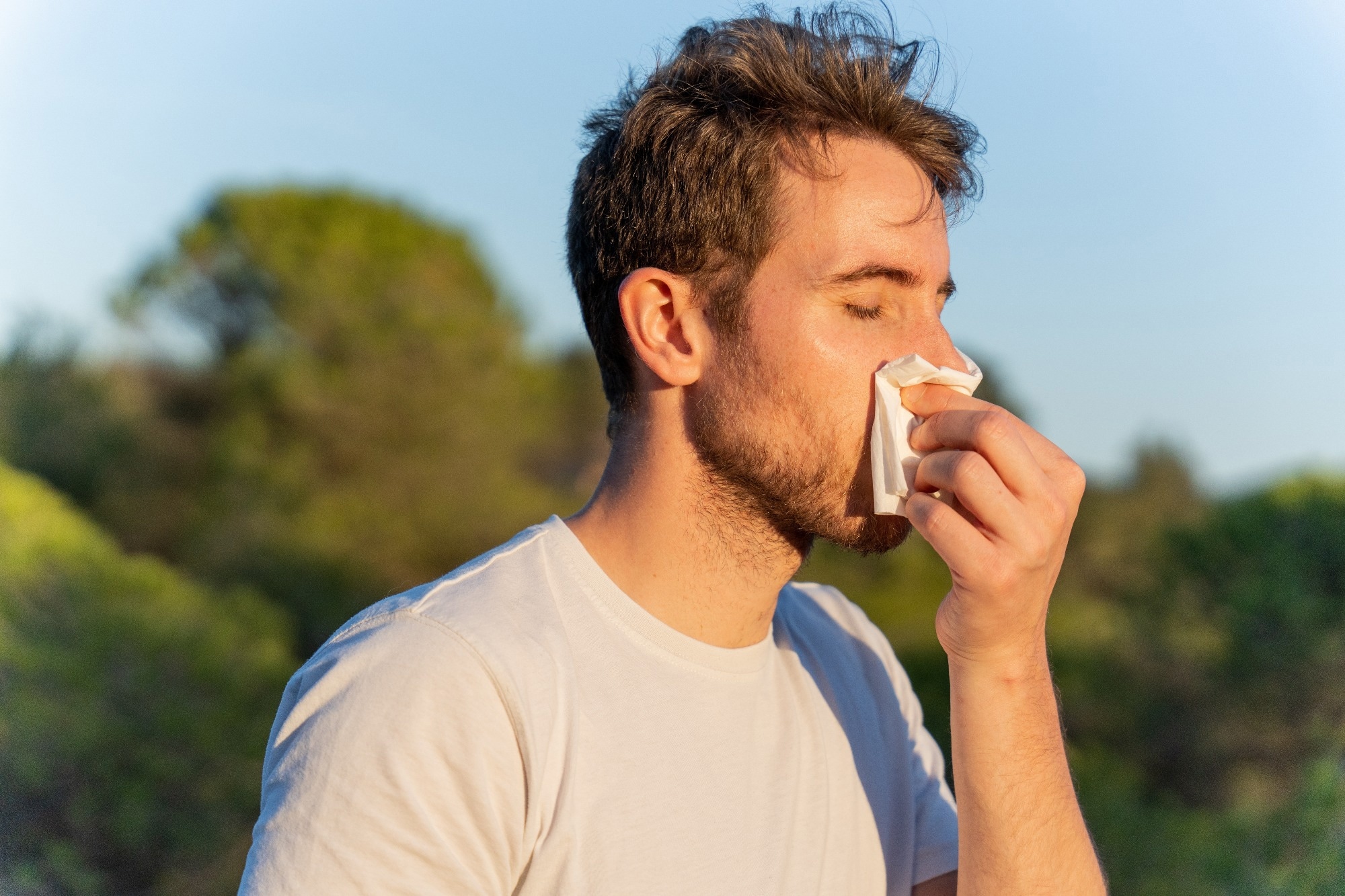 man surrounded by nature blowing his nose and sneezing for pollen allergy symptoms
