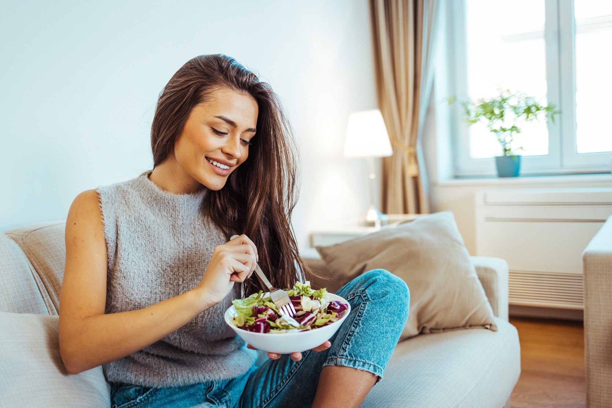 Close up portrait of young woman while she eats tasty vegan salad at home.