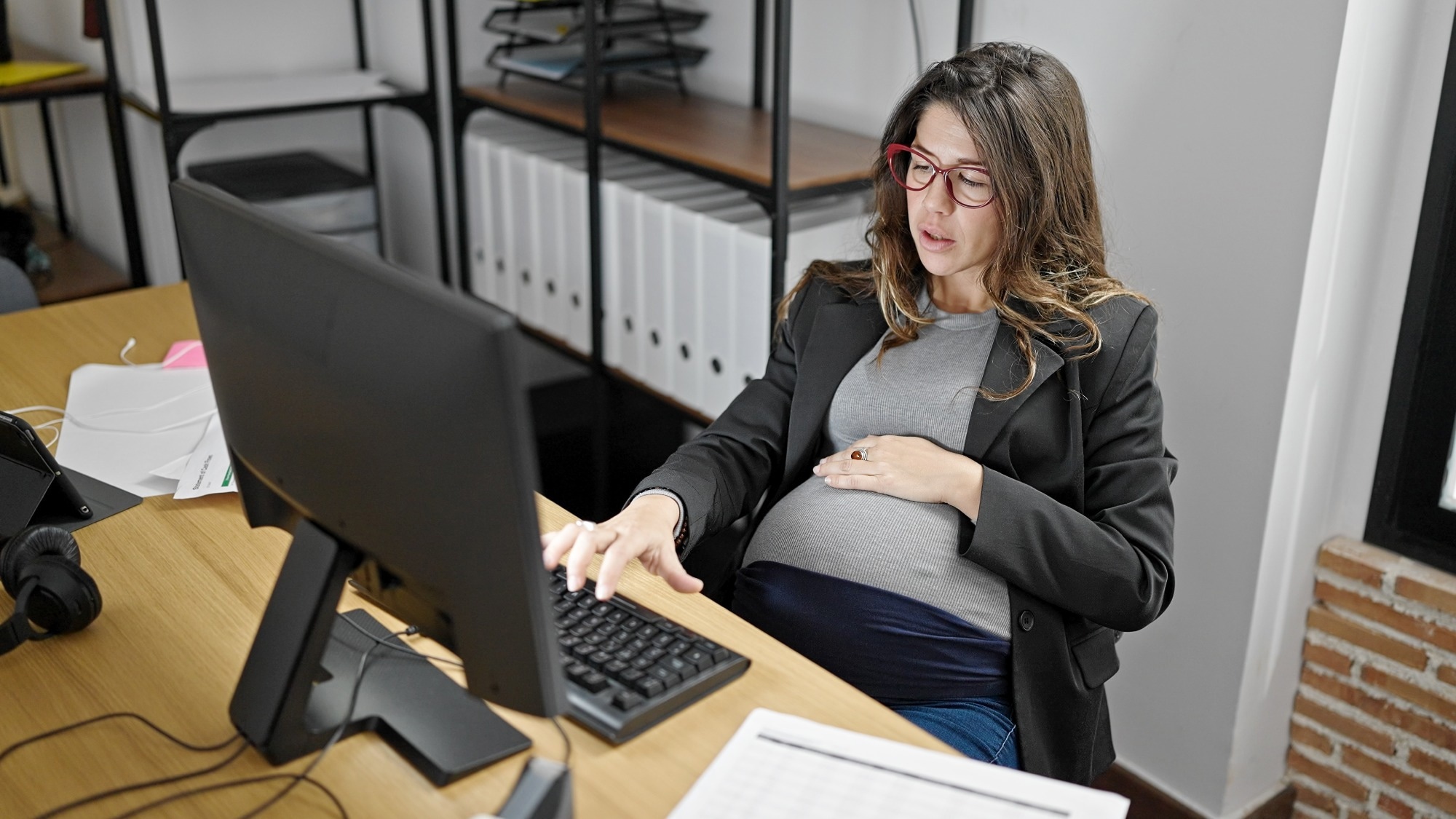 Young pregnant woman business worker using computer touching belly at office